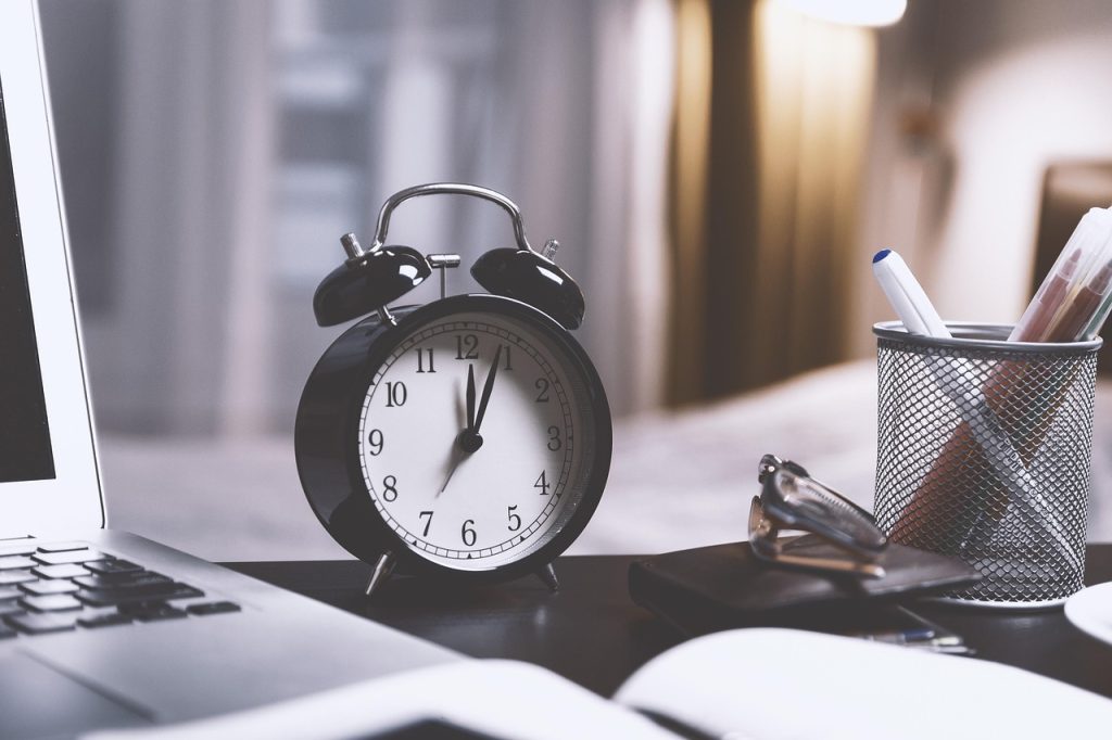 Budzik stojący obok laptopa symbolizuje upływ czasu oczekiwania na efekty pozycjonowania.